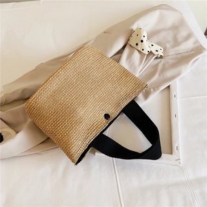 Detail of hand-woven straw tote with black strap and decorative circular button