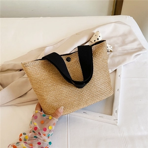 Detail of hand-woven straw tote bag with black fabric handles and snap button closure