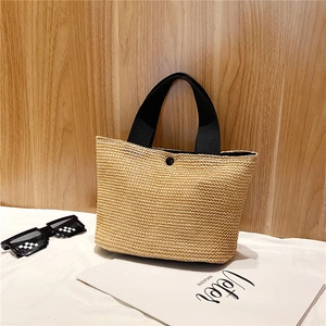 Detailed view of woven straw tote bag texture with black handles and metal button snap