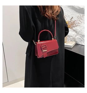 Deep red patent leather crossbody bag shown on model wearing black suit jacket