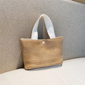 Detailed view of woven straw tote bag texture with white fabric handle and snap closure