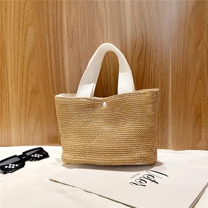 Close-up of woven straw handbag featuring white webbing handles and button closure