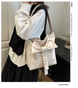 Detail of cream shoulder bag featuring silver studs on a large bow decoration