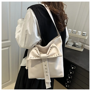 Detail view of cream PU leather shoulder bag featuring a large bow and silver studs