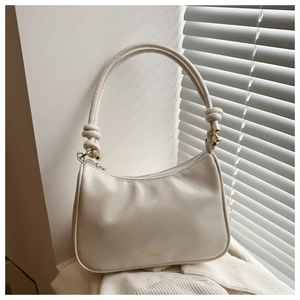 Gros plan du nœud et des ferrures dorées sur le sac fourre-tout minimaliste crème