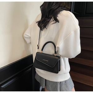 Detail of black textured handbag with adjustable strap and fashion lettering logo