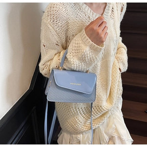 Detail of light blue textured leather handbag shown with crossbody strap on model outfit