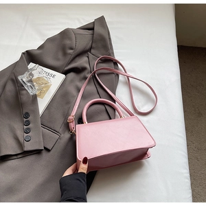 Pink faux leather trapezoid handbag placed on a grey blazer in a stylish urban setting