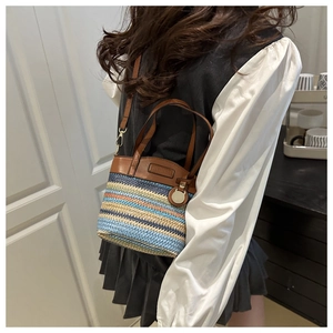 Detail of color-block woven straw bucket bag with brown leather trim and metal strap hooks