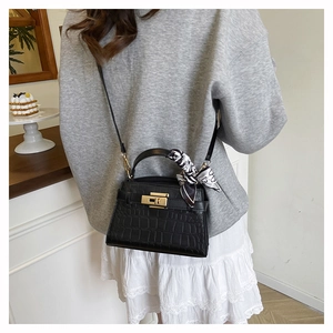 Detail of black crocodile texture handbag with gold metal lock and elegant floral scarf
