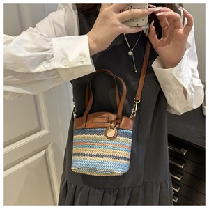 Detail of a rainbow woven crossbody bag featuring brown leather trim and metal hardware