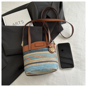 Detail of colorful woven straw bucket bag with leather handles and metallic charm