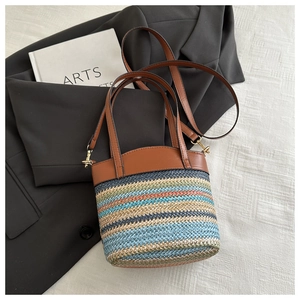 Close-up of colorful woven bucket bag with brown leather handles and gold metal hardware