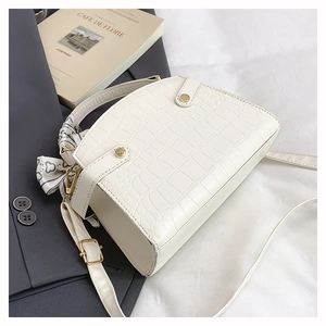 White crocodile pattern handbag with gold clasp and silk scarf handle detail on a suit