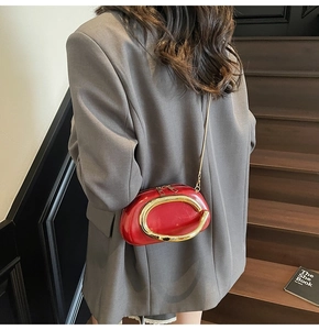 Detail of red leather mini bag with gold C-handle and chain strap on dark background