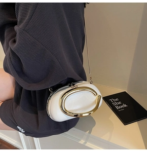 Detail of white leather bag featuring large gold C-shaped metal handle and slim chain strap
