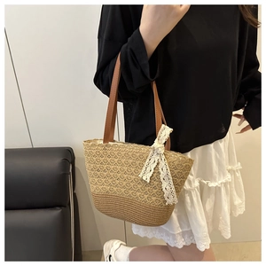 Close-up of woven straw tote bag featuring brown leather handles and a white lace bow detail