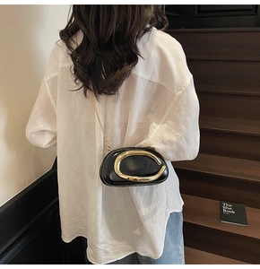 Detail of a chic black oval clutch with bold gold metal handle and chain shoulder strap