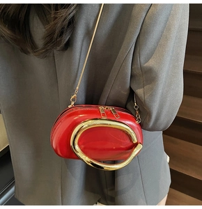 Close-up of bright red patent leather handbag with gold C-handle worn with grey blazer