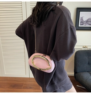 Pink oval evening bag with large gold metal ring handle and chain strap on model
