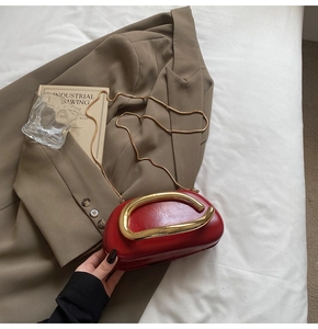 Detailed macro view of red patent leather clutch with a large gold U-shaped metal handle