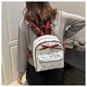 Rear view of a white backpack with red bow prints and shiny leather straps on a model