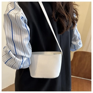 Close-up of a white bucket bag in textured leather with embossed logo and slim shoulder strap