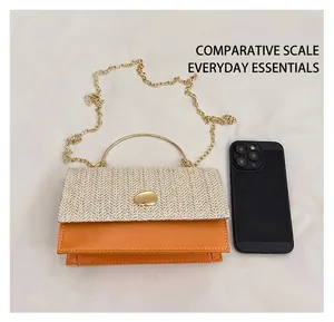 Detail of straw and orange leather crossbody bag with metal handle beside a smartphone