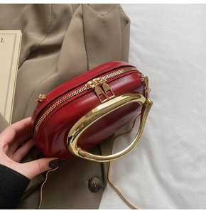Detail of red patent leather evening bag with large gold metal handle and chain strap