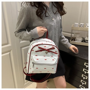 Close-up of white PU leather backpack featuring red bow prints and a metal heart pendant
