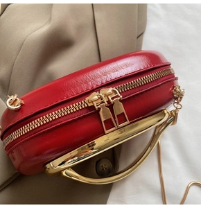 Close-up of red glossy leather evening bag with thick gold metal handle and dual zippers