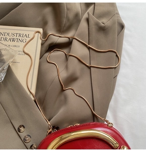 Detail of red glossy leather bag with gold metal handle and sleek snake chain strap