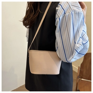 Close-up of minimalist beige PU leather crossbody bag with embossed logo on a model