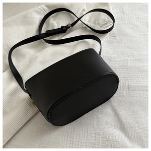 Top view of a black oval crossbody bucket bag with adjustable strap on white fabric