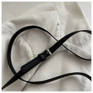 Close-up of thin black leather strap with silver metal buckle on white fabric background