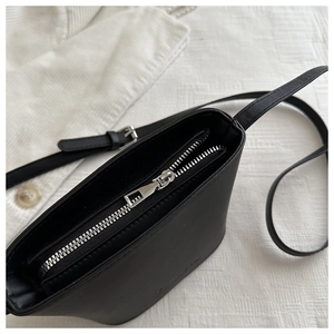 Close-up of smooth black faux leather crossbody bag showing silver zipper closure detail