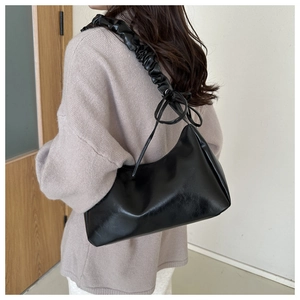 Close-up of black PU leather underarm bag featuring a ruched strap and bow detail