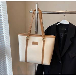 Detail of the high-capacity tote bag with brown straps and brand label on a display stand