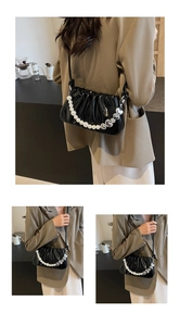 Detail of glossy black pleated cloud bag featuring pearl and silver heart chain strap