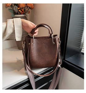 Detail of dark brown leather bucket bag with geometric strap and gold-tone hardware