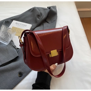 Close-up of a deep red glossy leather shoulder bag with a square gold metal buckle