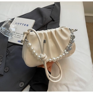 Detail of cream pleated cloud bag featuring a large pearl chain and silver heart pendant