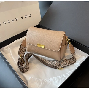 Macro shot of khaki leather bag with wide ethnic pattern strap in gift packaging