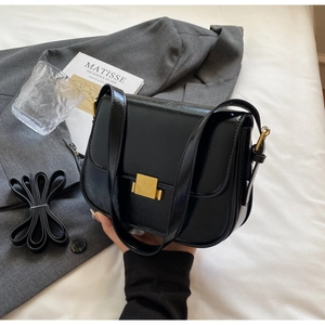 Detail of a black patent leather square bag with a golden metallic push-lock closure