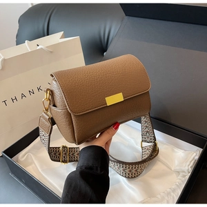 Detail of brown litchi leather bag with gold buckle and wide geometric woven strap