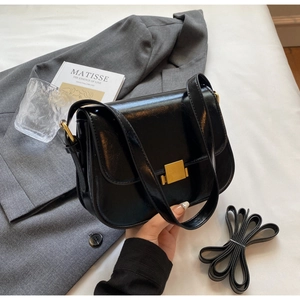Detail of black square bag with glossy leather texture and gold metal buckle closure