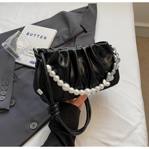 Close-up of black pleated cloud bag with elegant pearl and silver heart chain detail