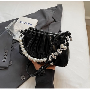 Detail of glossy black pleated underarm bag with pearl chain and heart charms