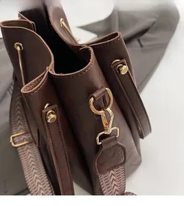Detail of dark brown bucket bag featuring gold ring hardware and vintage woven strap