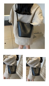 Detailed side view and brand embossing on a black leather bucket bag with adjustable strap